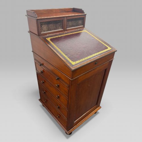 fig 1. An antique mahogany Davenport desk featuring a sloped red leather writing surface, turned drawer knobs, and a top gallery superstructure.