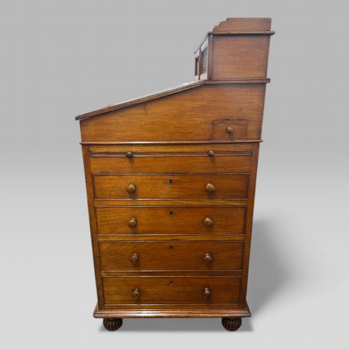 fig 2. An antique mahogany Davenport desk featuring a sloped red leather writing surface, turned drawer knobs, and a top gallery superstructure.