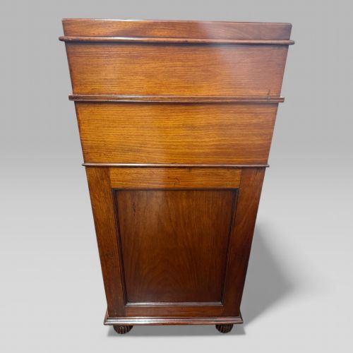 fig 3. An antique mahogany Davenport desk featuring a sloped red leather writing surface, turned drawer knobs, and a top gallery superstructure.
