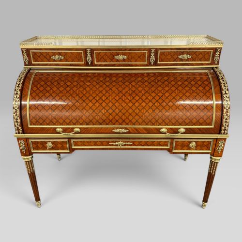 fig 1. A French Louis XVI style cylinder desk featuring detailed geometric diamond parquetry, gilded bronze mounts, a top brass gallery rail, and slender fluted legs.