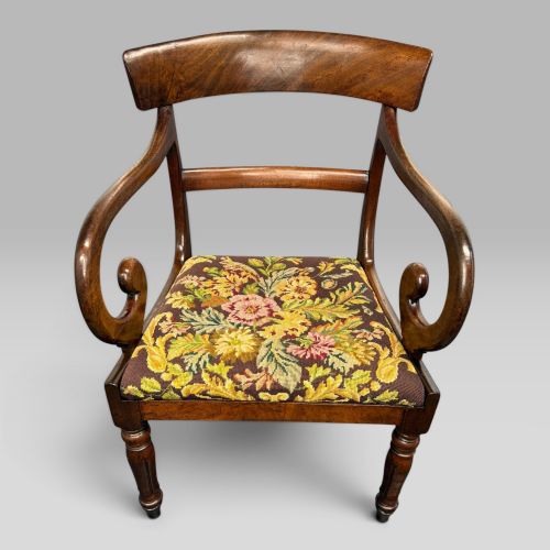 fig 1. An antique William IV mahogany elbow armchair featuring scrolled armrests, turned front legs, and a floral tapestry upholstered seat.