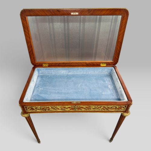 fig 4. A rectangular French Louis XVI style bijouterie display table featuring a glazed glass top, decorative gilt bronze mounts along the frieze, and slender tapered legs ending in brass sabots.