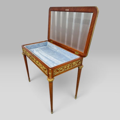 fig 5. A rectangular French Louis XVI style bijouterie display table featuring a glazed glass top, decorative gilt bronze mounts along the frieze, and slender tapered legs ending in brass sabots.