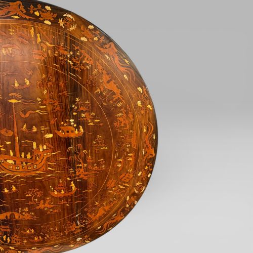 fig 5. A circular dark rosewood centre table featuring detailed marquetry inlays depicting ships, pagodas, and flora.