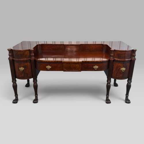 fig 1. An antique Regency flame mahogany sideboard featuring a breakfront top, reeded columns, brass ring handles, and six carved lion paw feet.