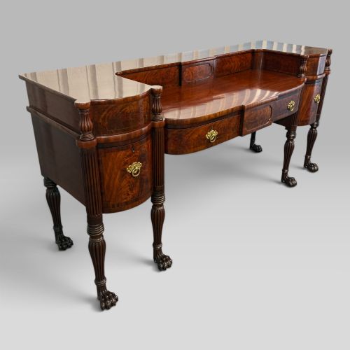 fig 2. An antique Regency flame mahogany sideboard featuring a breakfront top, reeded columns, brass ring handles, and six carved lion paw feet.