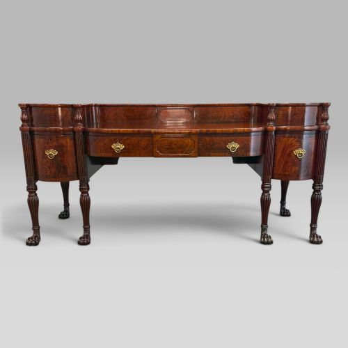fig 3. An antique Regency flame mahogany sideboard featuring a breakfront top, reeded columns, brass ring handles, and six carved lion paw feet.