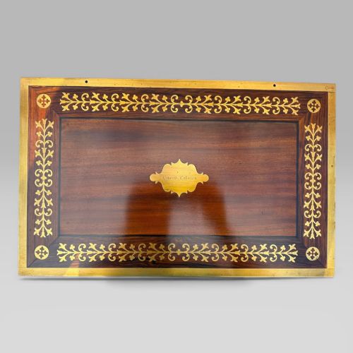 fig 4. A rectangular mahogany and rosewood writing slope featuring brass bound edges, foliate brass inlay borders, a keyhole escutcheon, and an engraved brass cartouche.