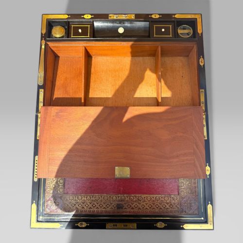 fig 6. A rectangular mahogany and rosewood writing slope featuring brass bound edges, foliate brass inlay borders, a keyhole escutcheon, and an engraved brass cartouche.