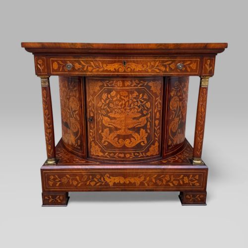 fig 3. An antique Dutch mahogany console cabinet heavily decorated with intricate floral marquetry, featuring a single drawer above a rounded central cupboard door, flanked by turned columns.