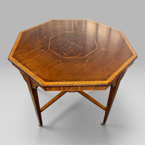 fig 2. An octagonal Edwardian mahogany centre table featuring floral marquetry inlays, satinwood crossbanded borders, tapered legs, an X-stretcher, and brass castors.