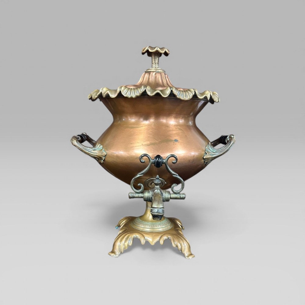 An antique Victorian copper samovar featuring a fluted lid, scalloped brass rim, cast brass side handles, a brass spigot, and a four-footed scroll base.