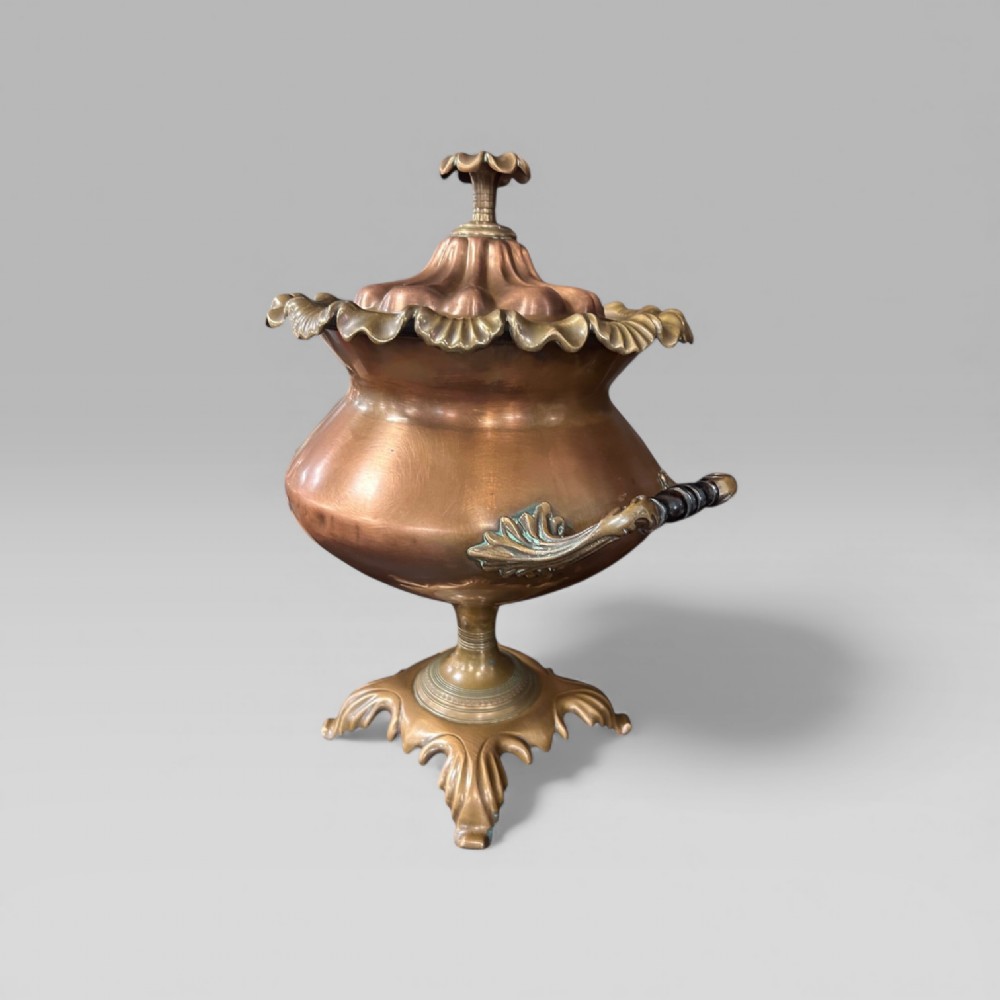 An antique Victorian copper samovar featuring a fluted lid, scalloped brass rim, cast brass side handles, a brass spigot, and a four-footed scroll base. View V