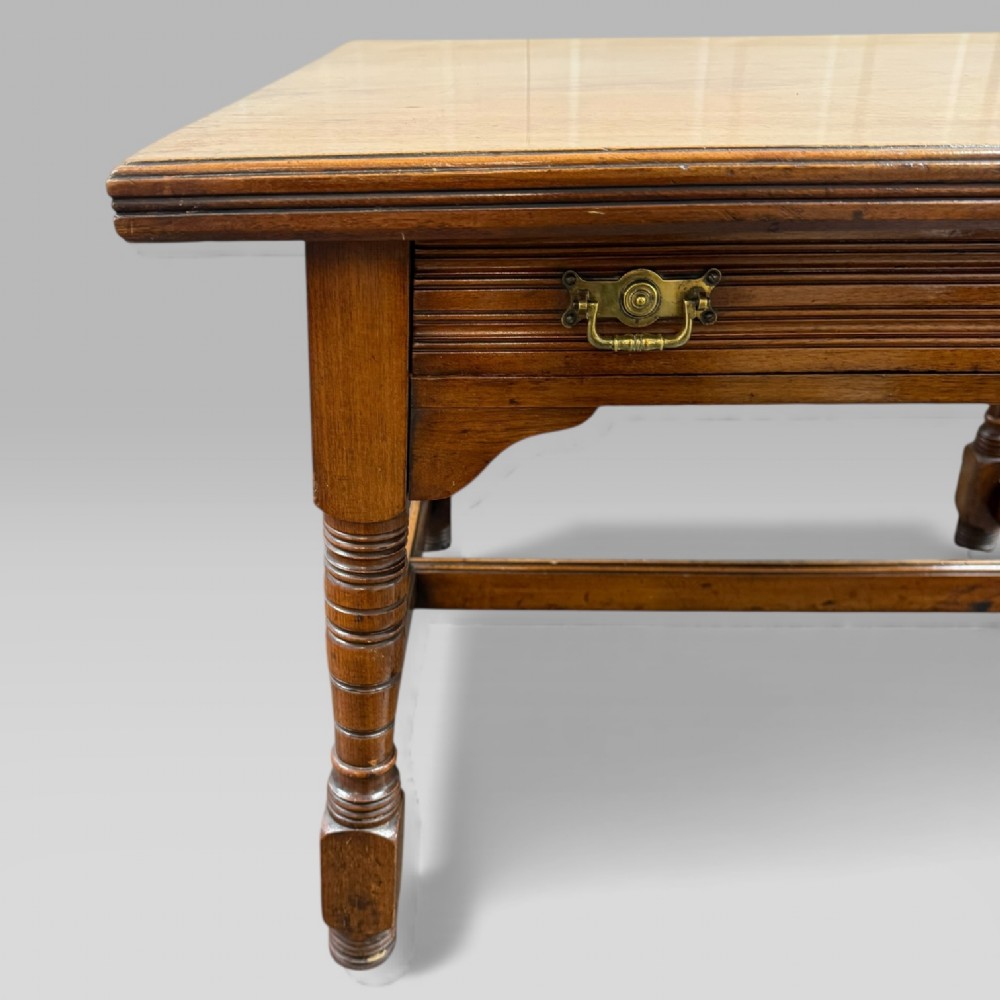 An antique walnut coffee table featuring turned legs, a rectangular top, brass drop handles, and an H-stretcher base. View IV