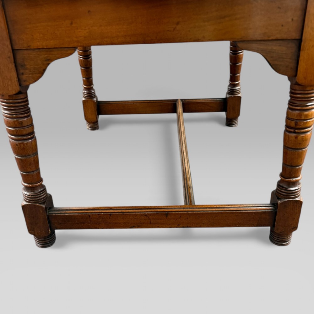 An antique walnut coffee table featuring turned legs, a rectangular top, brass drop handles, and an H-stretcher base. View XV