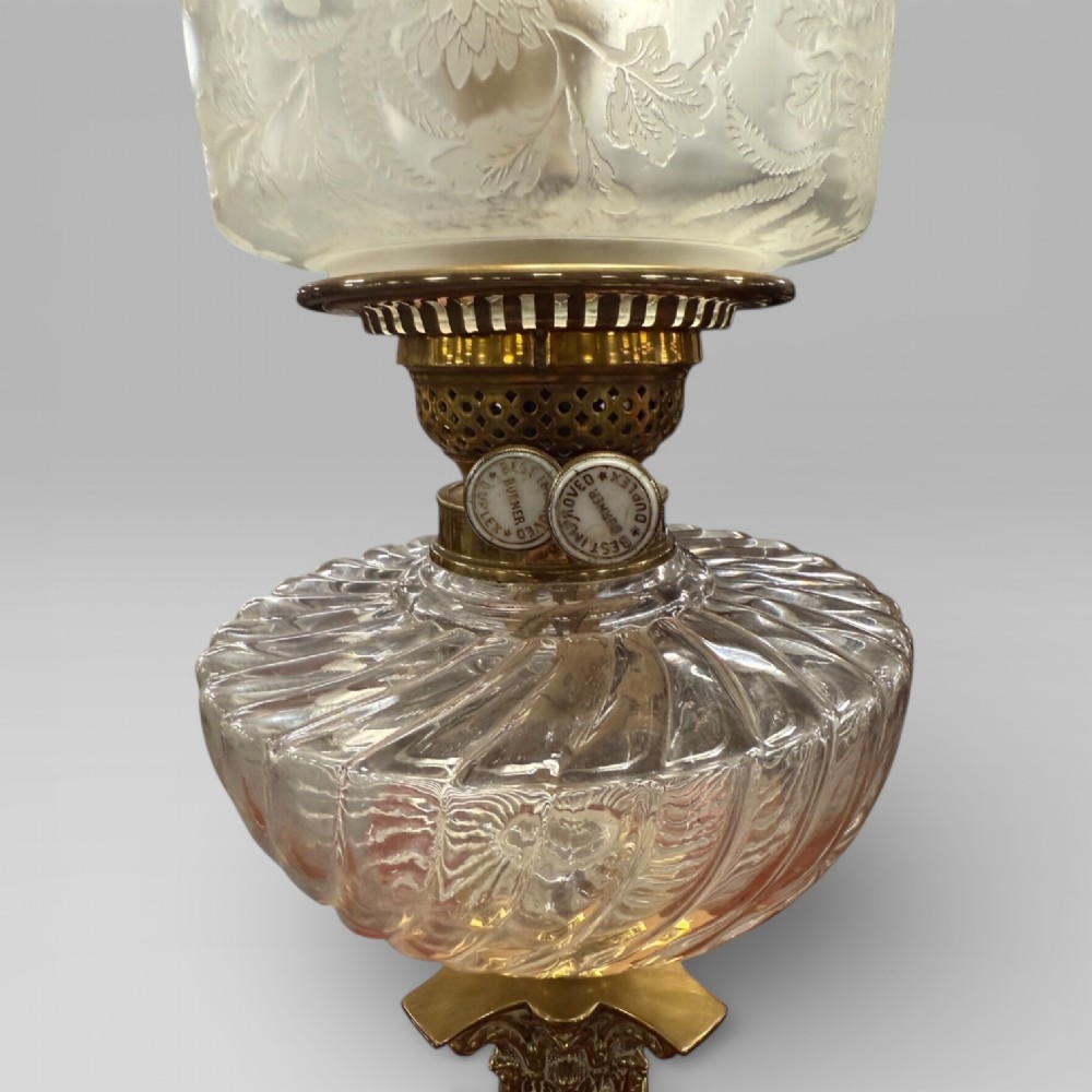 An antique Victorian oil lamp featuring a Corinthian style brass column base, clear glass reservoir, and an etched glass tulip shade with a frilled top rim. View VII