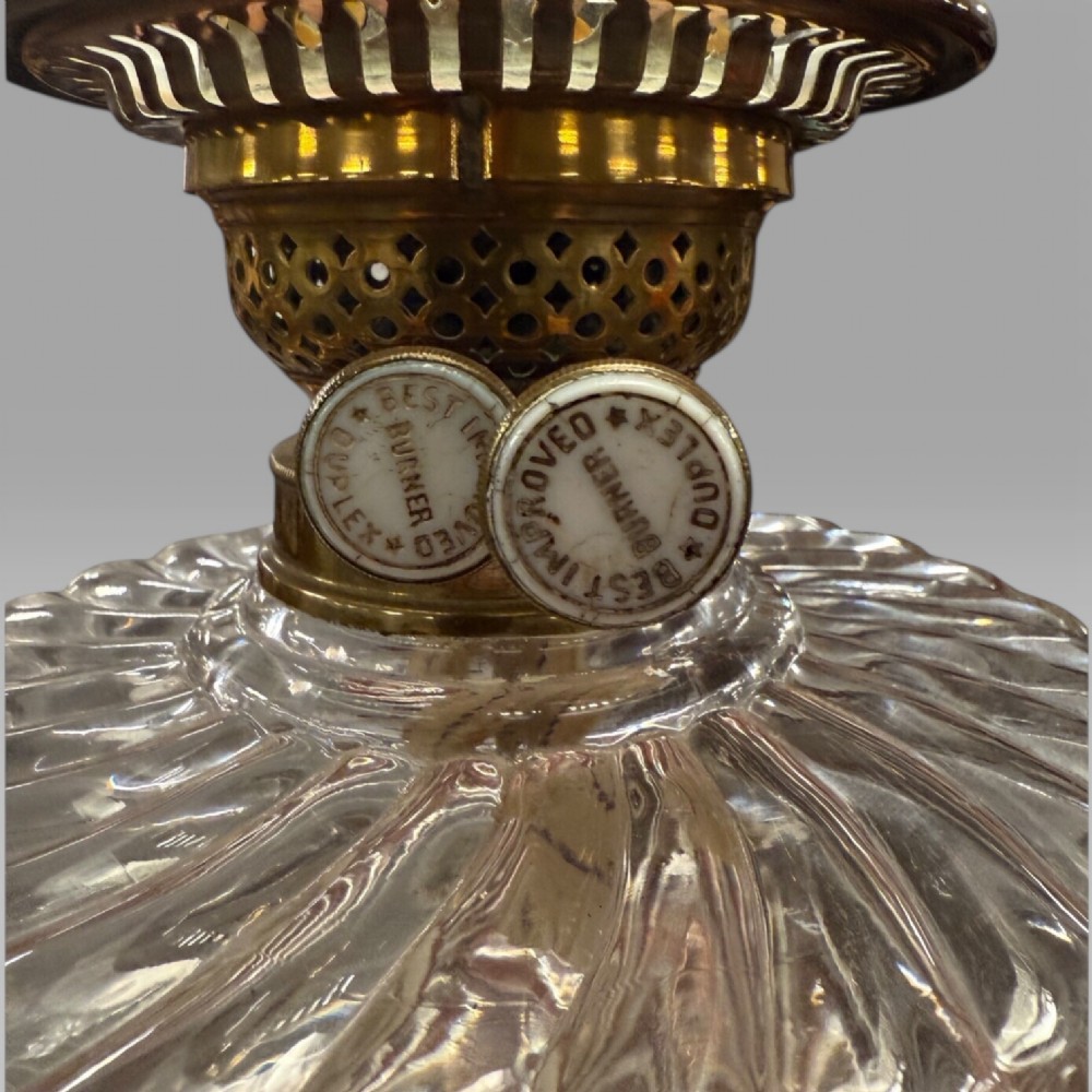 An antique Victorian oil lamp featuring a Corinthian style brass column base, clear glass reservoir, and an etched glass tulip shade with a frilled top rim. View X