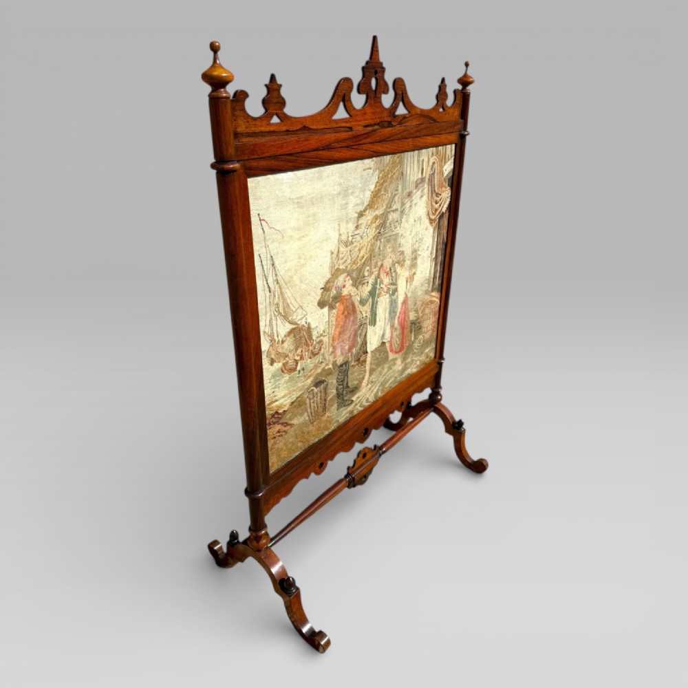 A Victorian rosewood cheval fire screen featuring a carved wooden frame with finials and an embroidered textile panel depicting figures near a coastal cottage. View III