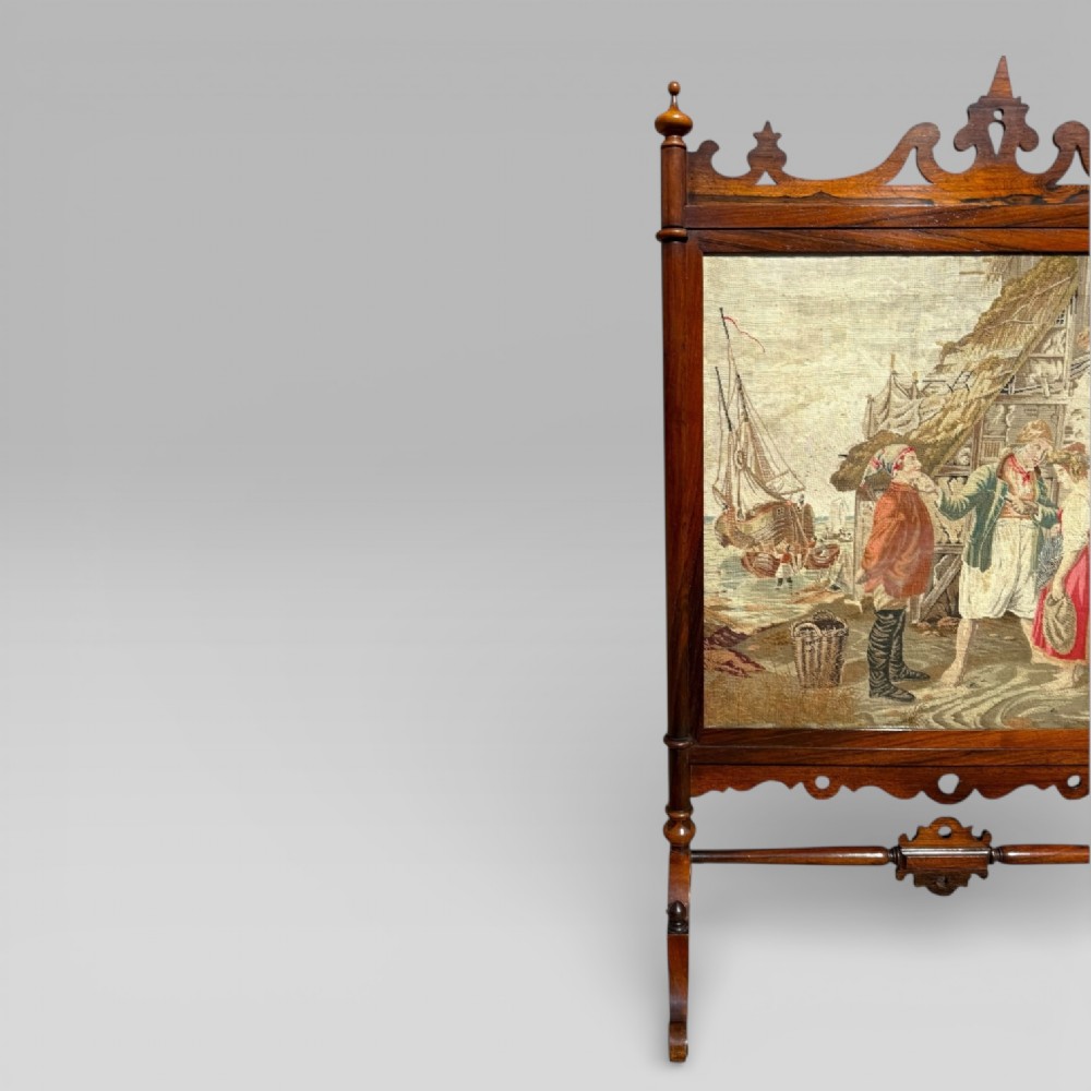 A Victorian rosewood cheval fire screen featuring a carved wooden frame with finials and an embroidered textile panel depicting figures near a coastal cottage. View IV