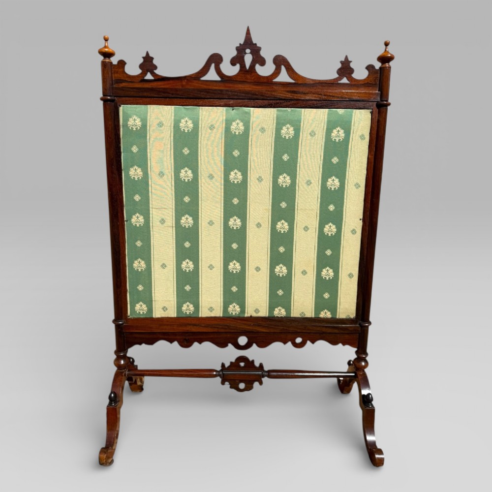 A Victorian rosewood cheval fire screen featuring a carved wooden frame with finials and an embroidered textile panel depicting figures near a coastal cottage. View VII