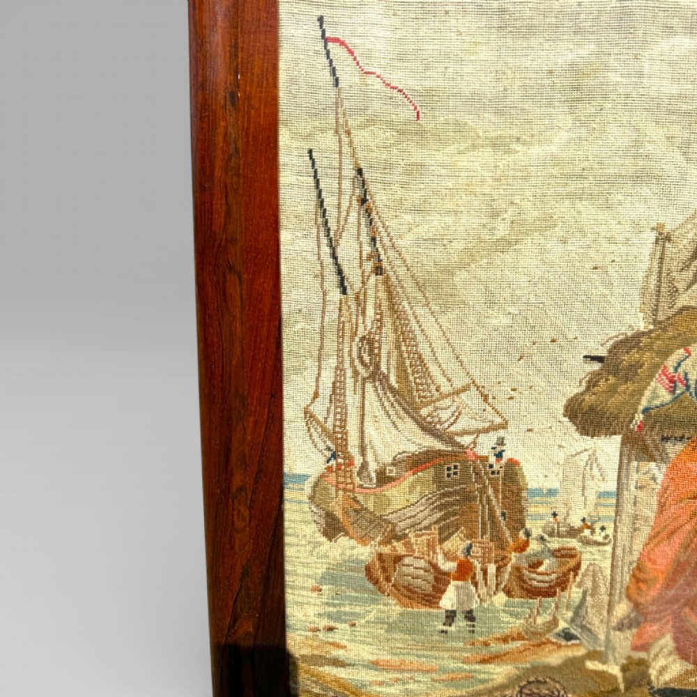 A Victorian rosewood cheval fire screen featuring a carved wooden frame with finials and an embroidered textile panel depicting figures near a coastal cottage. View XI