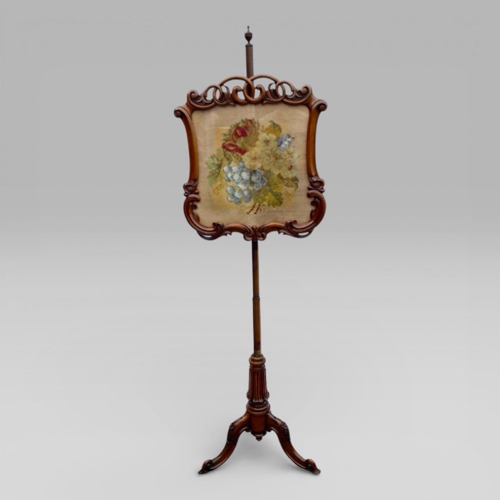 An antique Victorian rosewood pole screen featuring a carved floral tapestry panel mounted on an adjustable central column with a carved tripod base.