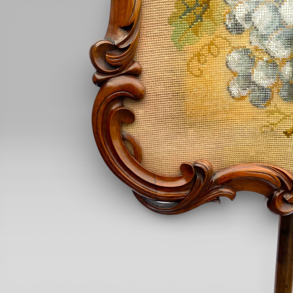 An antique Victorian rosewood pole screen featuring a carved floral tapestry panel mounted on an adjustable central column with a carved tripod base. View IV
