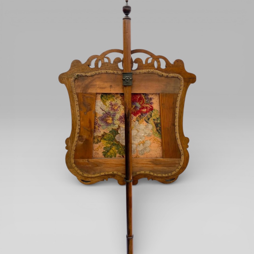 An antique Victorian rosewood pole screen featuring a carved floral tapestry panel mounted on an adjustable central column with a carved tripod base. View V