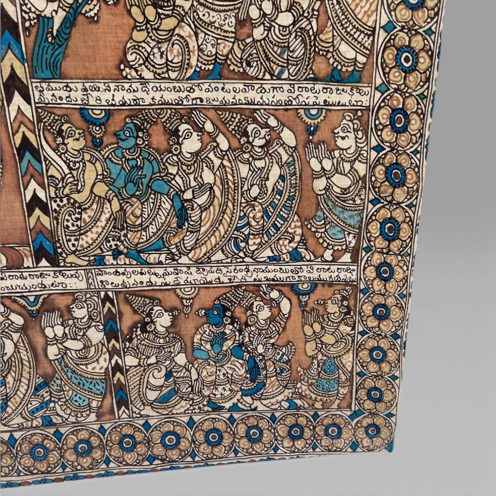A rectangular Indian Kalamkari cotton textile displaying narrative panels filled with hand-drawn Hindu deities framed by a decorative floral border in blue, beige, and terracotta tones. View X