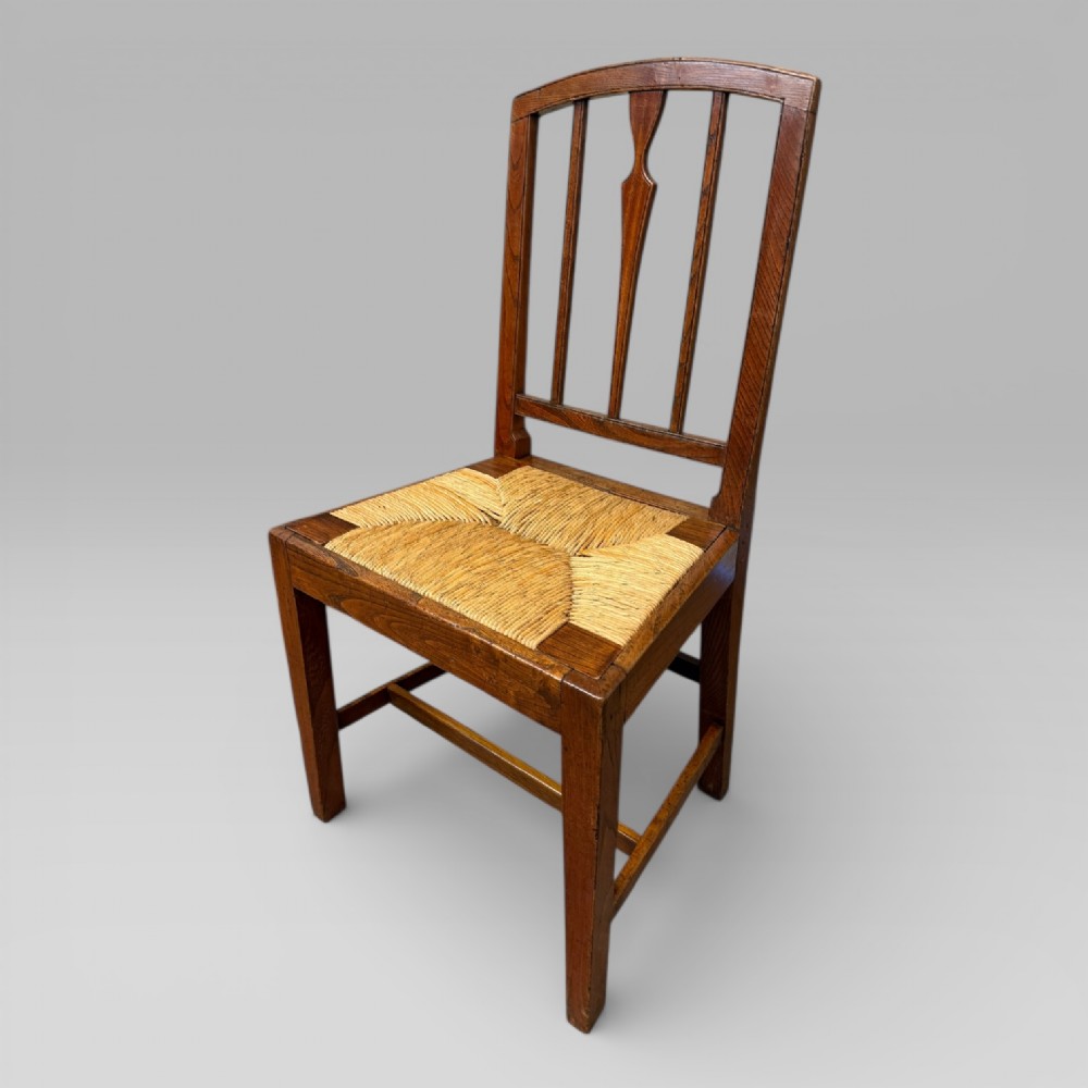A 19th-century elm side chair featuring a woven rush seat, vertical back slats, and straight legs connected by stretchers.