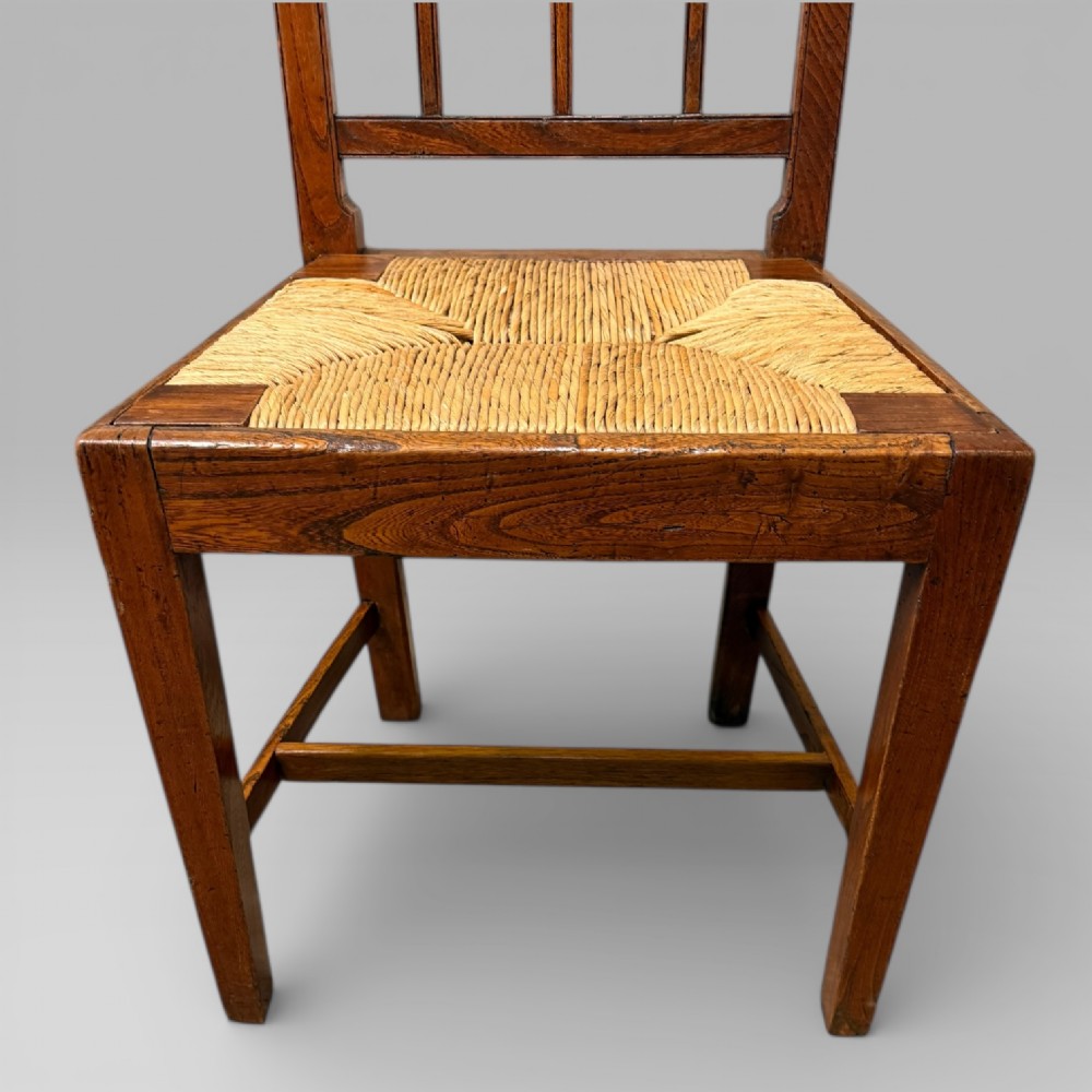 A 19th-century elm side chair featuring a woven rush seat, vertical back slats, and straight legs connected by stretchers. View VII