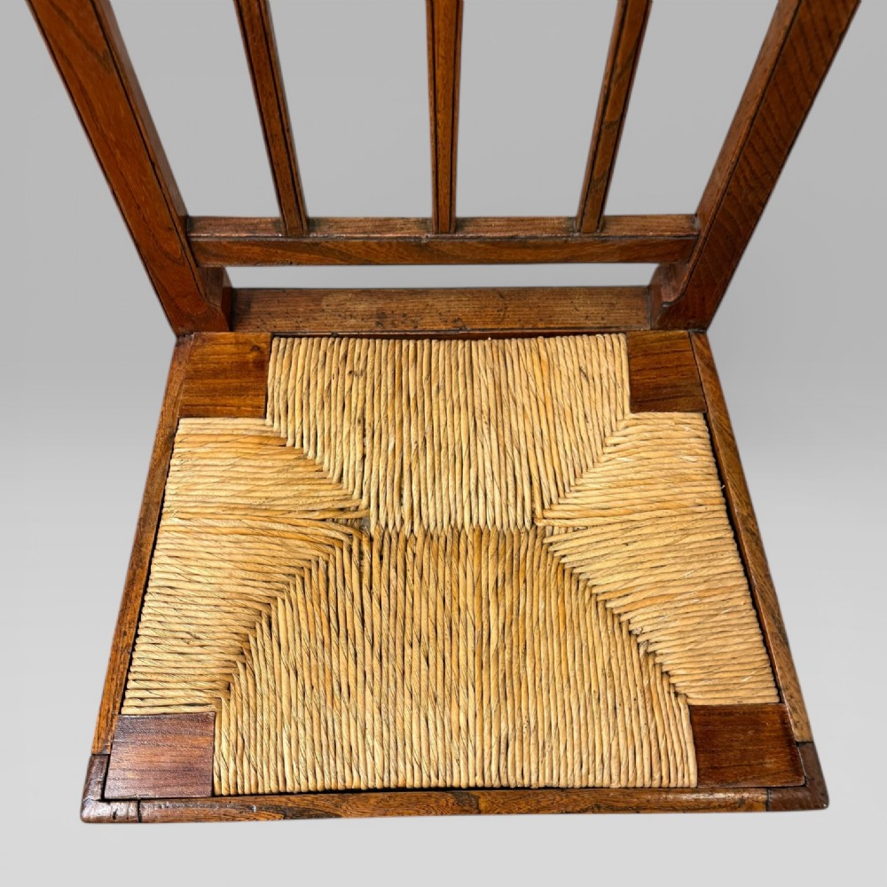 A 19th-century elm side chair featuring a woven rush seat, vertical back slats, and straight legs connected by stretchers. View X