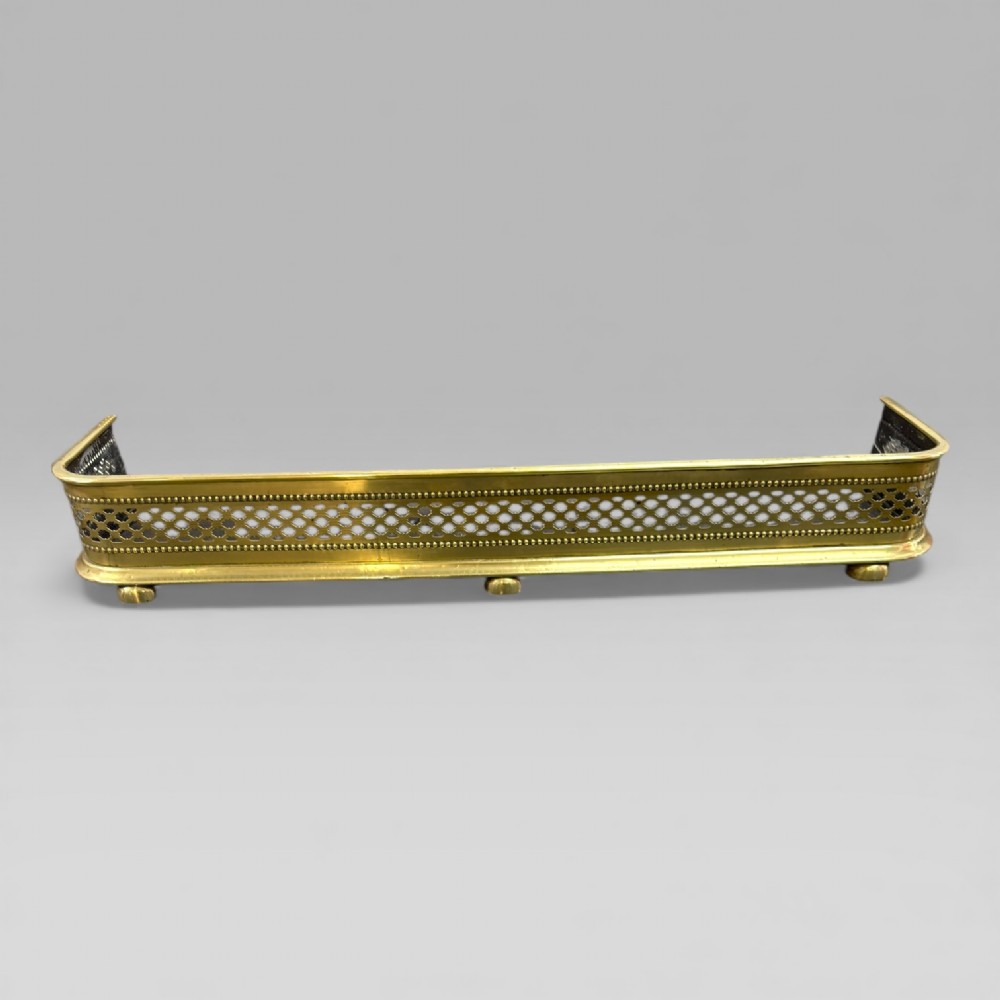 A long Victorian brass fire fender featuring a pierced lattice pattern, beaded edge trim, and low support feet.