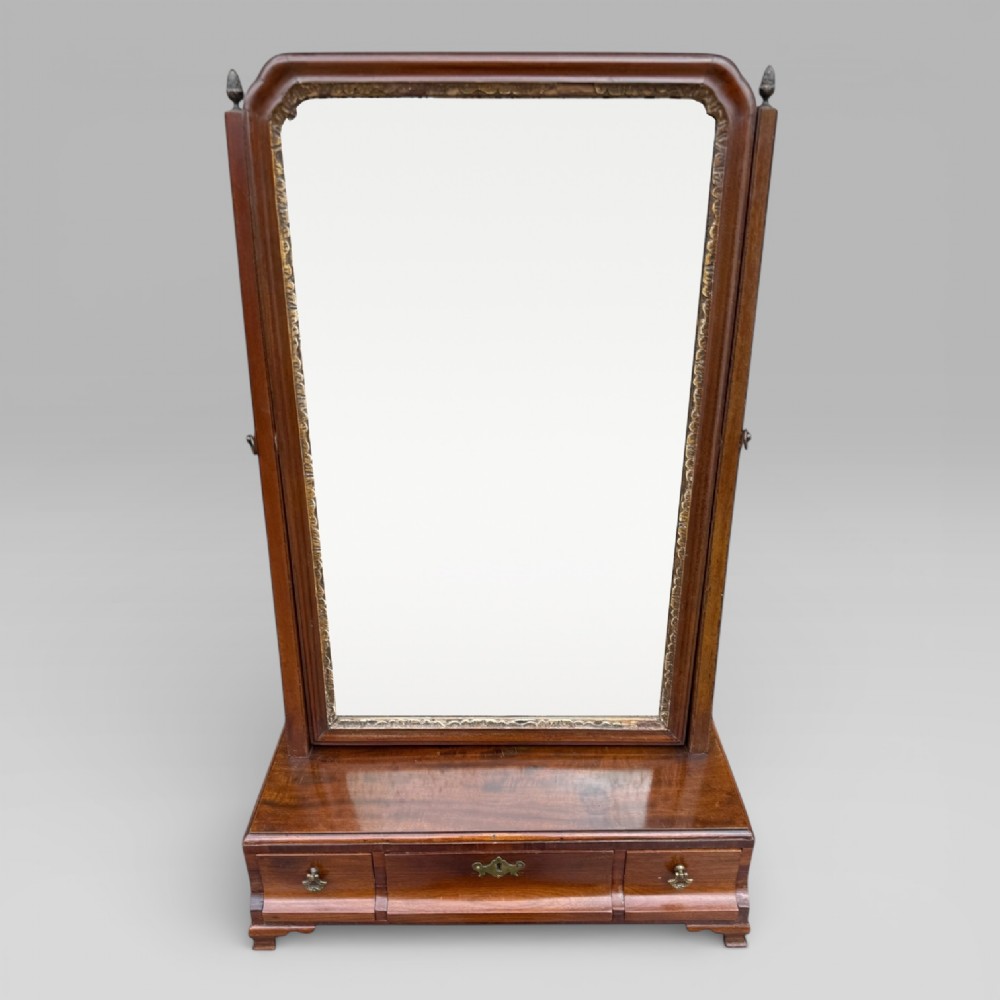 An 18th-century Georgian mahogany dressing table mirror featuring an arched glass frame with a gilt inner slip, brass finials, and a plinth base fitted with drawers.