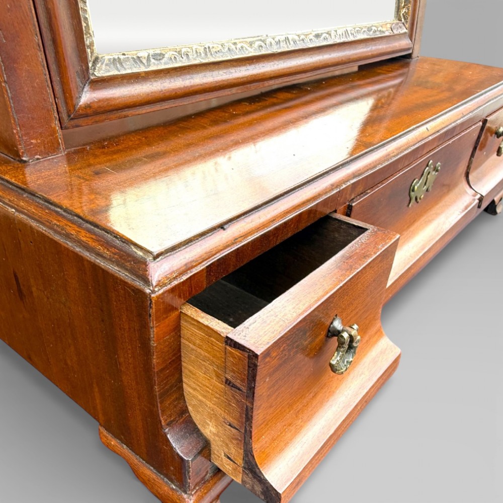 An 18th-century Georgian mahogany dressing table mirror featuring an arched glass frame with a gilt inner slip, brass finials, and a plinth base fitted with drawers. View IV