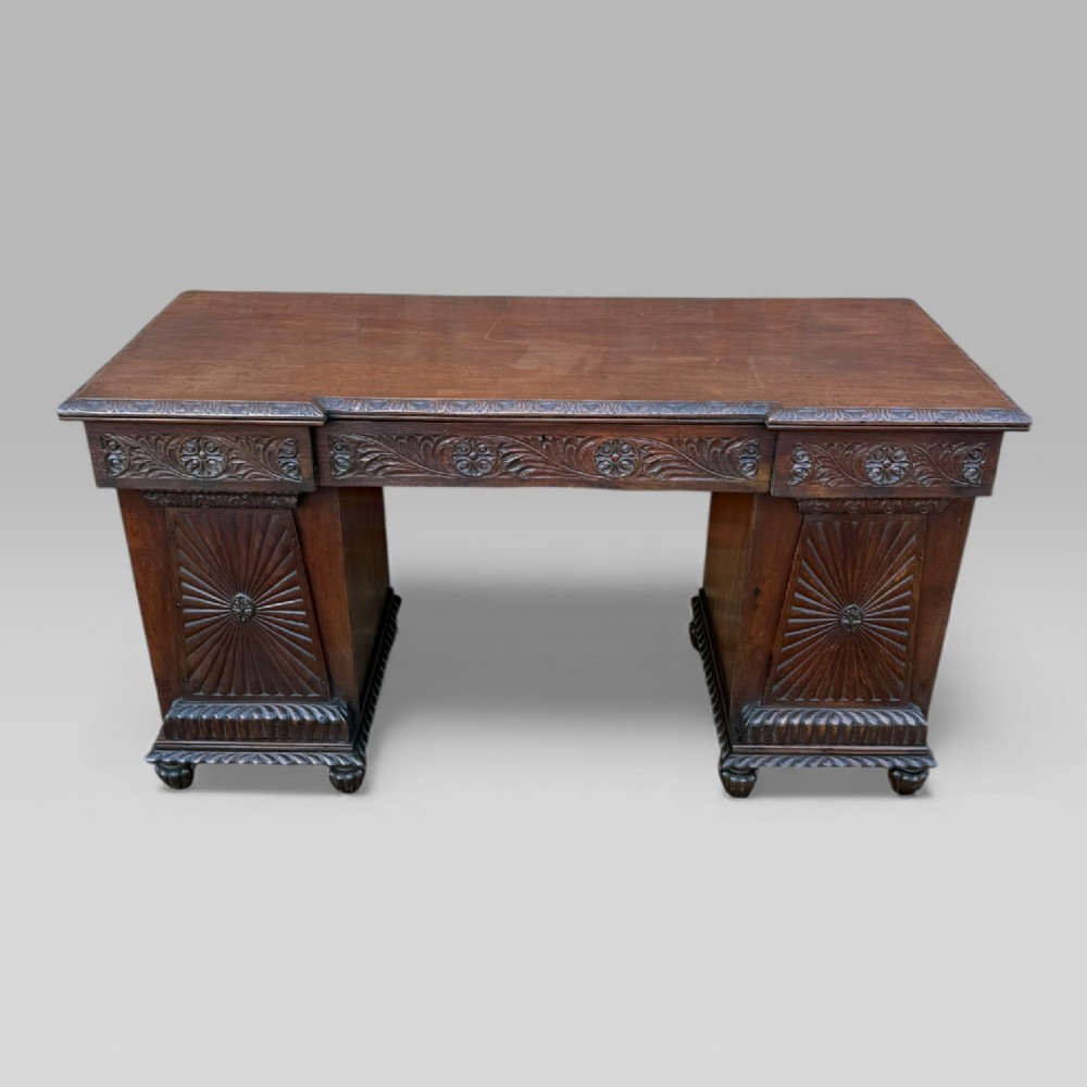 A dark carved padouk wood sideboard featuring intricate floral frieze carvings, sunburst panel pedestals, and a central kneehole design.
