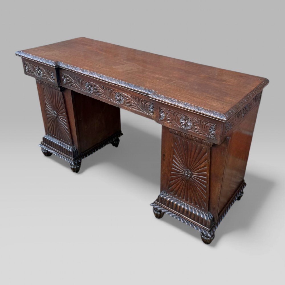 A dark carved padouk wood sideboard featuring intricate floral frieze carvings, sunburst panel pedestals, and a central kneehole design. View II