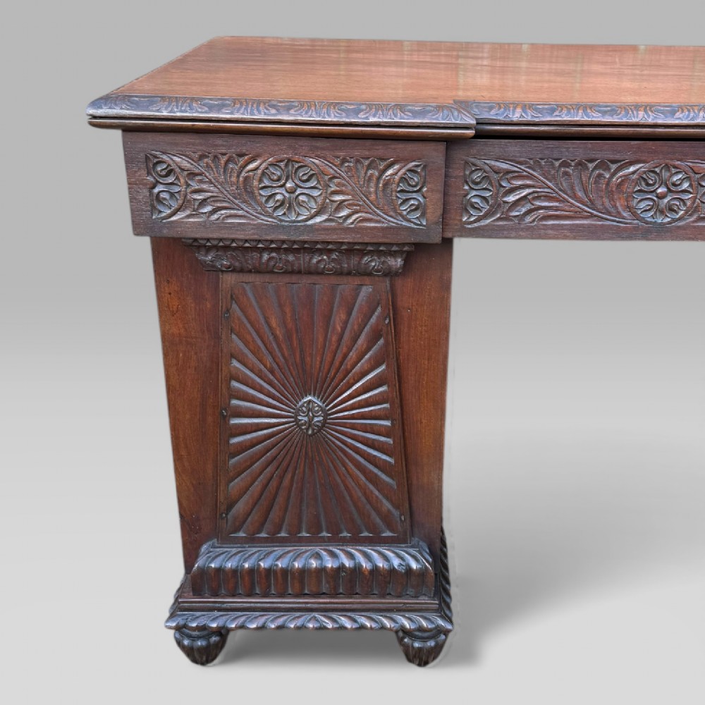A dark carved padouk wood sideboard featuring intricate floral frieze carvings, sunburst panel pedestals, and a central kneehole design. View VI