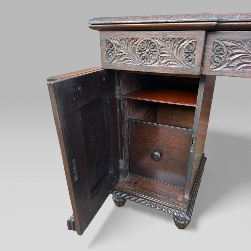 A dark carved padouk wood sideboard featuring intricate floral frieze carvings, sunburst panel pedestals, and a central kneehole design. View XIII