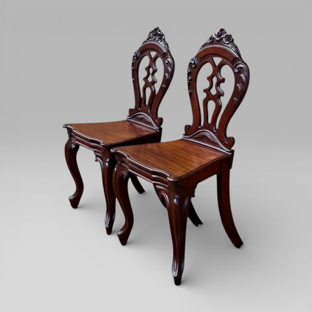 A matching pair of antique Victorian mahogany hall chairs featuring carved pierced backrests, solid wooden seats, and cabriole front legs. View II