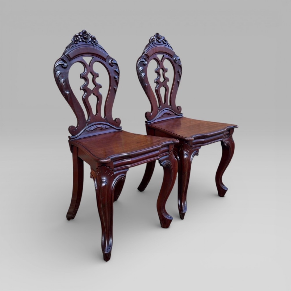 A matching pair of antique Victorian mahogany hall chairs featuring carved pierced backrests, solid wooden seats, and cabriole front legs. View III