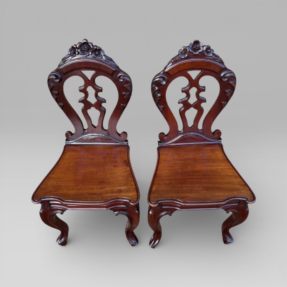 A matching pair of antique Victorian mahogany hall chairs featuring carved pierced backrests, solid wooden seats, and cabriole front legs. View IV