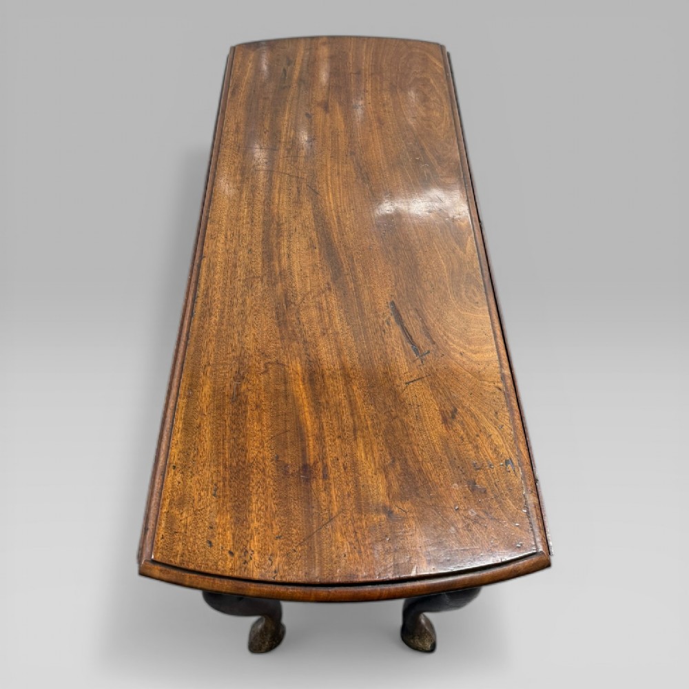 An 18th-century George II mahogany drop-leaf table with hinged oval flaps, cabriole legs terminating in pad feet, and a side drawer with a brass handle. View IV