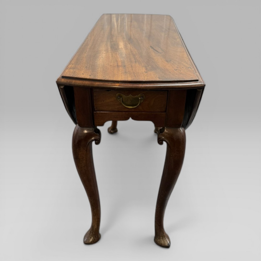An 18th-century George II mahogany drop-leaf table with hinged oval flaps, cabriole legs terminating in pad feet, and a side drawer with a brass handle. View V