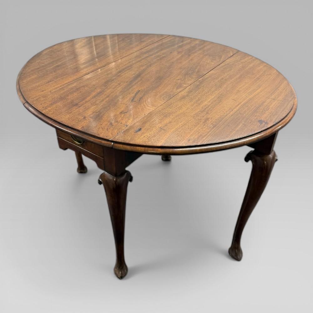 An 18th-century George II mahogany drop-leaf table with hinged oval flaps, cabriole legs terminating in pad feet, and a side drawer with a brass handle. View VII