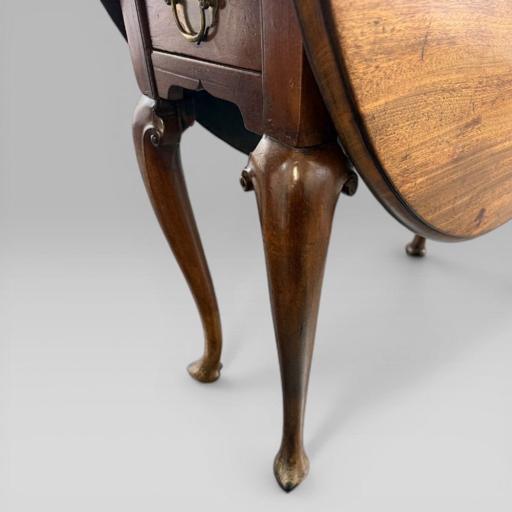 An 18th-century George II mahogany drop-leaf table with hinged oval flaps, cabriole legs terminating in pad feet, and a side drawer with a brass handle. View IX