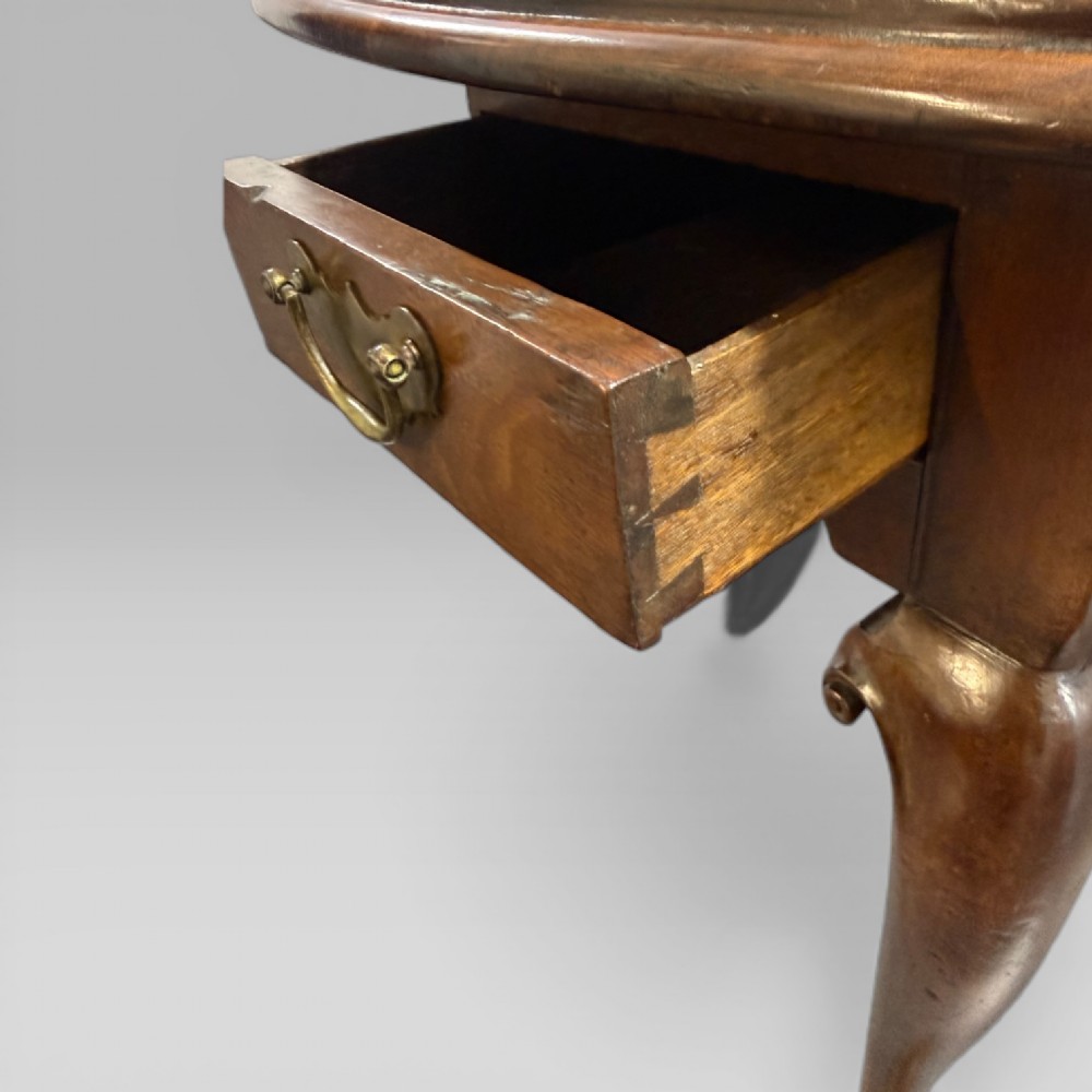 An 18th-century George II mahogany drop-leaf table with hinged oval flaps, cabriole legs terminating in pad feet, and a side drawer with a brass handle. View X