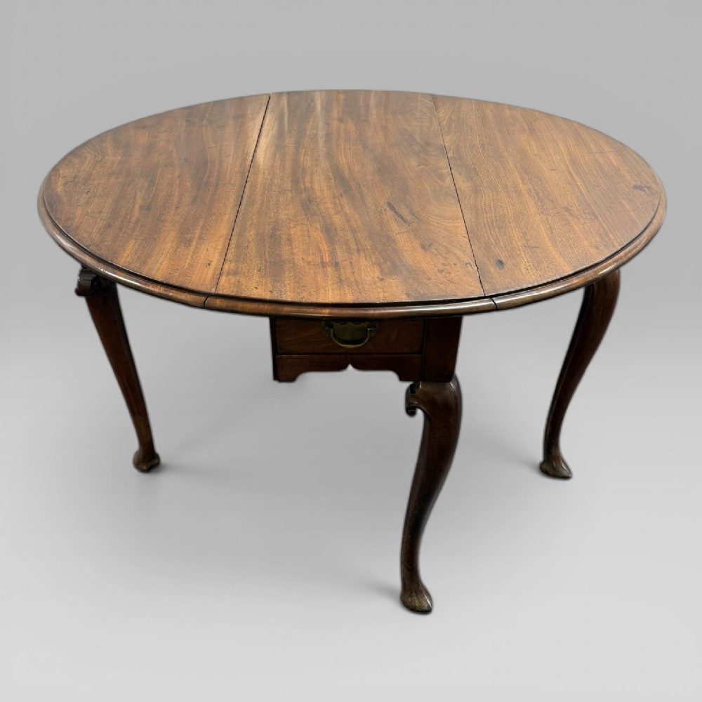An 18th-century George II mahogany drop-leaf table with hinged oval flaps, cabriole legs terminating in pad feet, and a side drawer with a brass handle. View XIII
