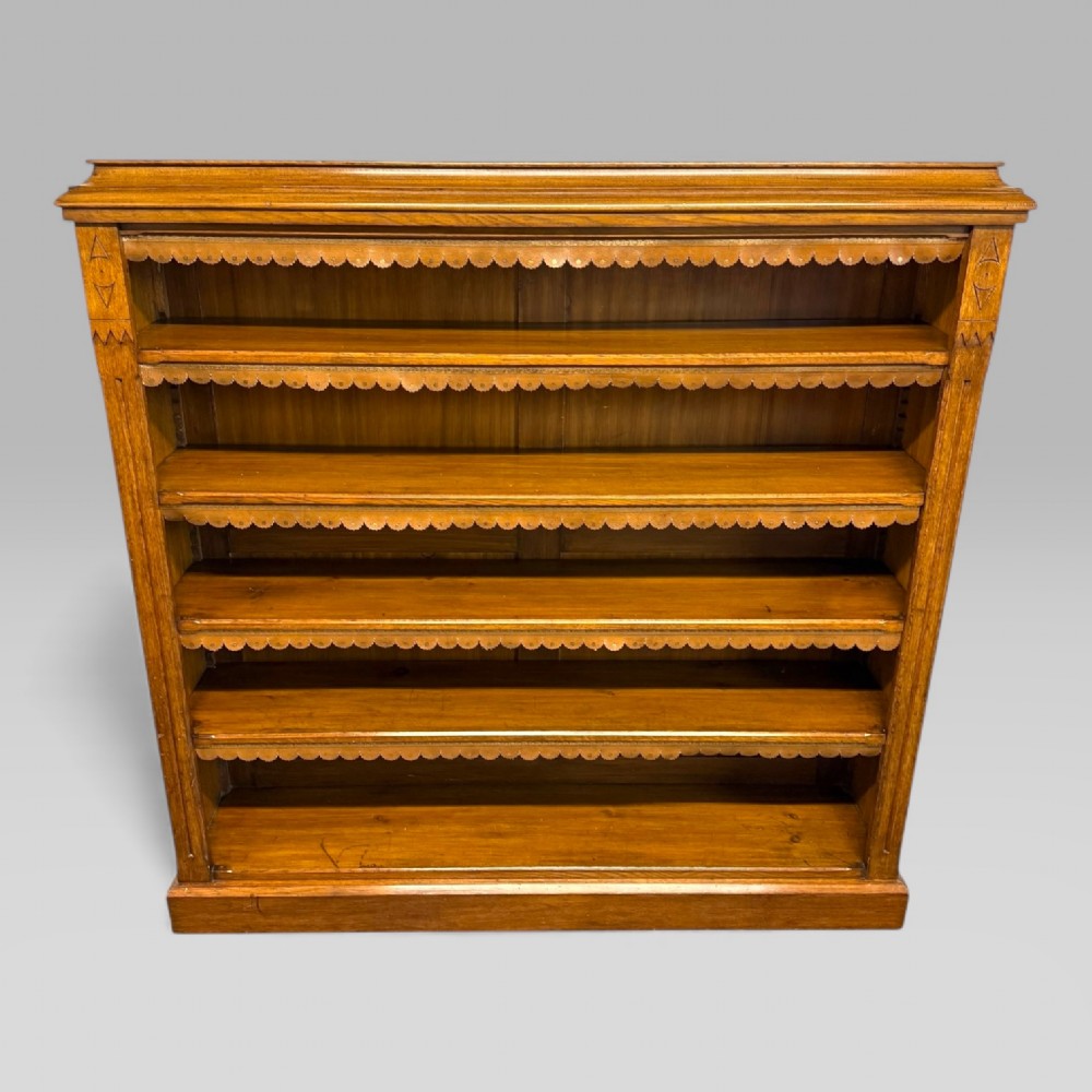 A late Victorian open bookcase crafted from golden oak, featuring scalloped edging along each shelf and subtle geometric carvings on the pilasters. View II
