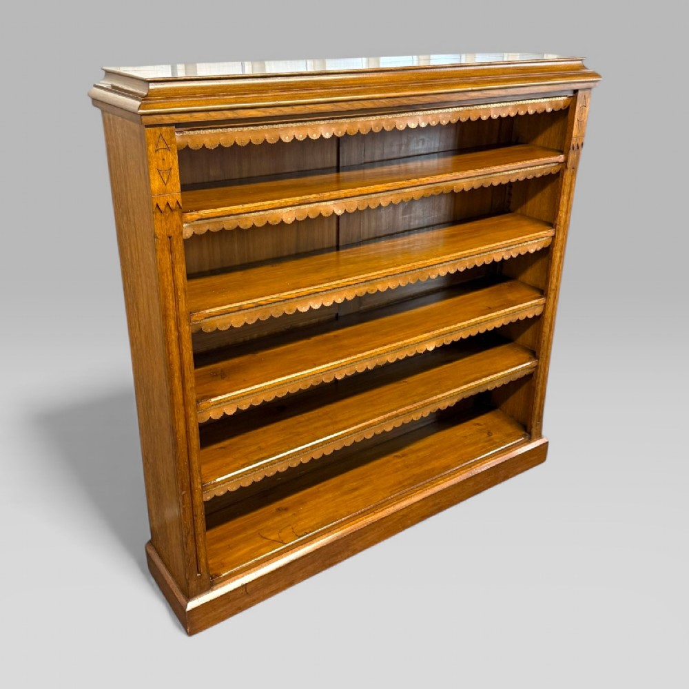A late Victorian open bookcase crafted from golden oak, featuring scalloped edging along each shelf and subtle geometric carvings on the pilasters. View V